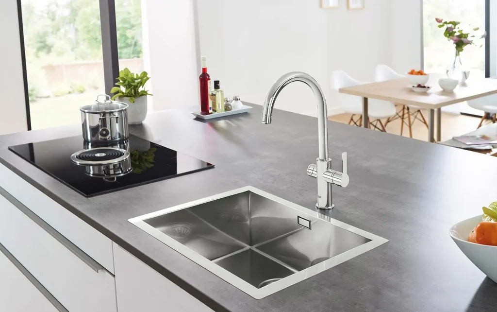 Moderne Küchenarbeitsplatte mit Edelstahlspüle, elegantem Wasserhahn und Induktionskochfeld, im Hintergrund ist ein Essbereich zu sehen.