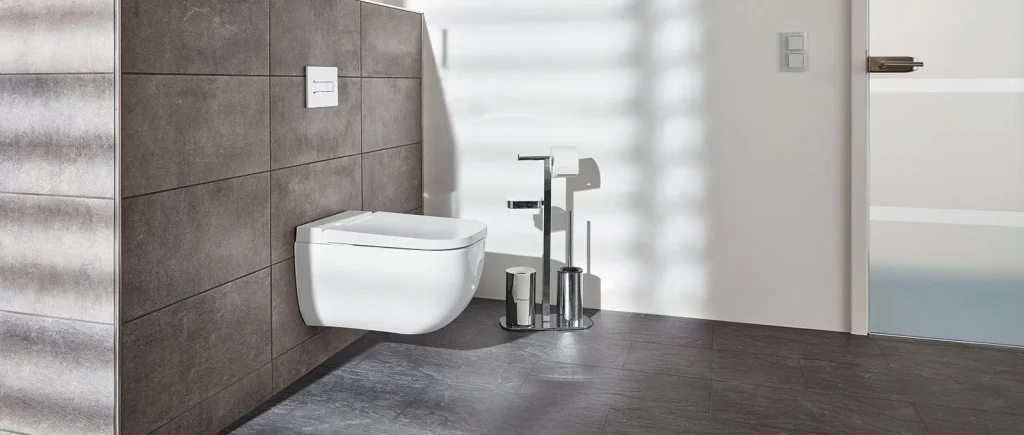 Ein modernes Badezimmer mit wandhängender Toilette vor dunklen Strukturfliesen. Sonnenlicht wirft Streifen auf den Boden und erzeugt so eine ruhige, minimalistische Atmosphäre.