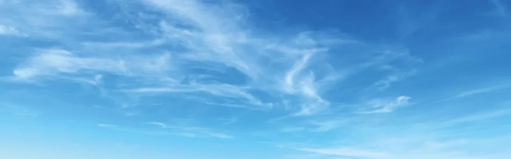 Strahlend blauer Himmel mit zarten weißen Wolken. Die Szene vermittelt eine ruhige und heitere Atmosphäre und deutet auf einen klaren, sonnigen Tag hin.