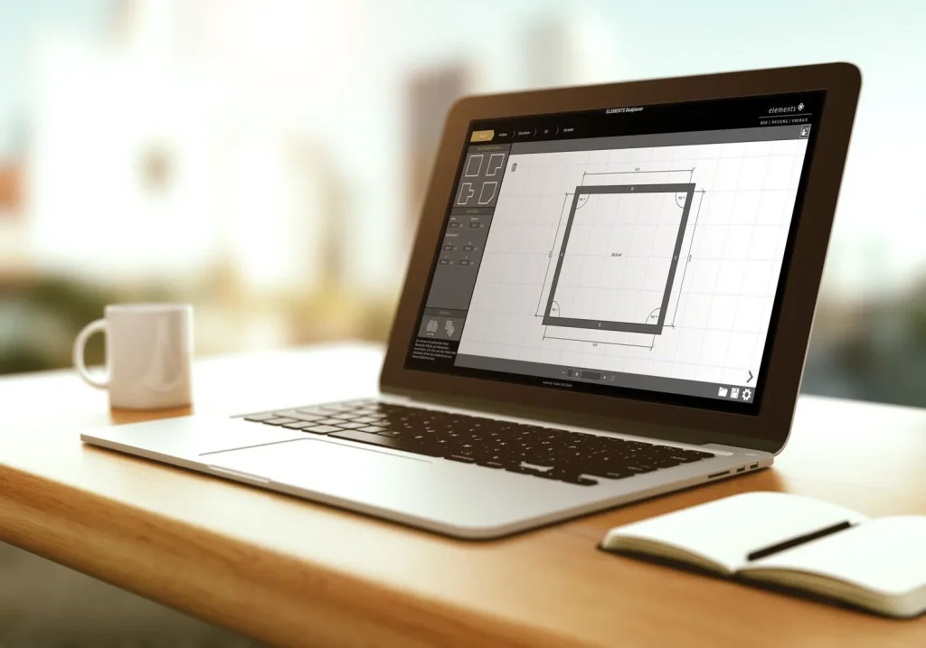 Auf einem Holzschreibtisch steht ein Laptop, auf dessen Bildschirm ein technisches Design dargestellt ist. Daneben sorgen eine weiße Tasse und ein Notizbuch mit Stift für eine Arbeitsatmosphäre.